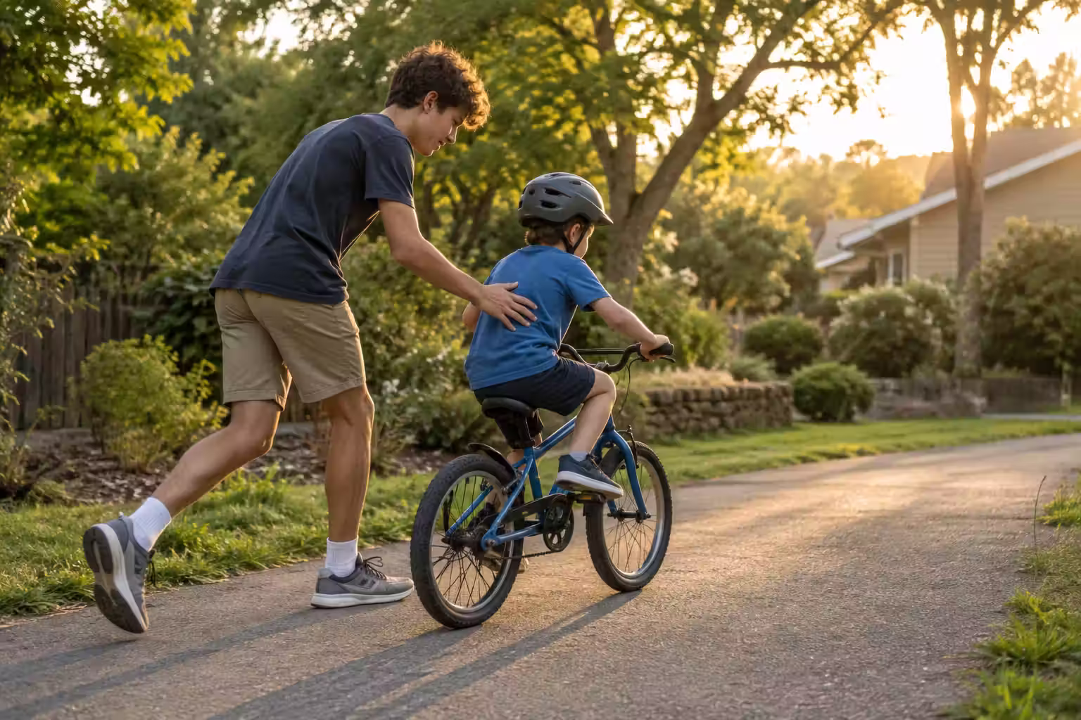 An older brother helping a younger brother practice riding a bicycle on a quiet path