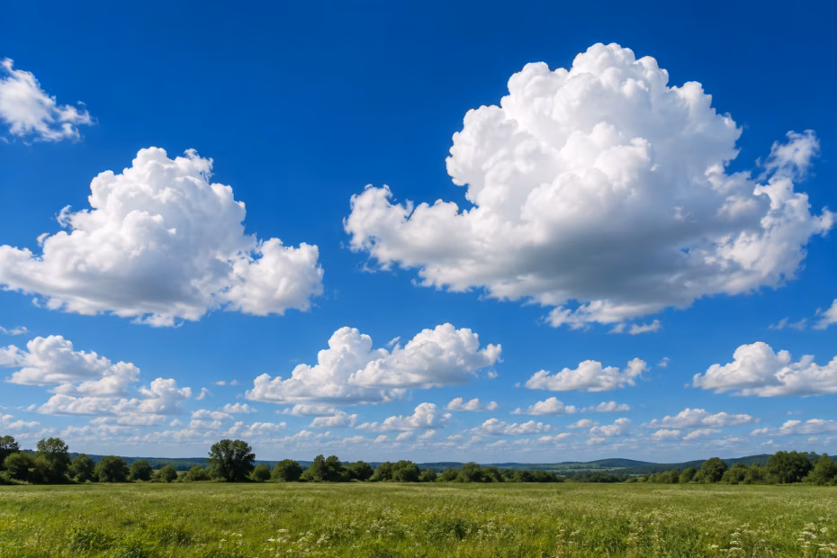Sunlit white cumulus clouds build above a green landscape in a blue sky.