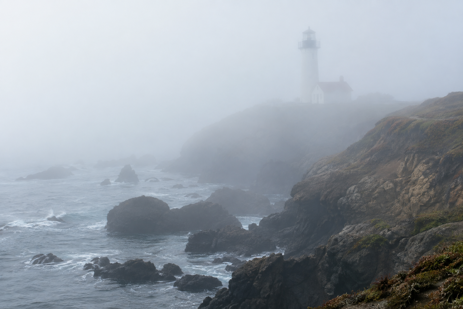 A coastal headland and lighthouse partly obscured by sea fog