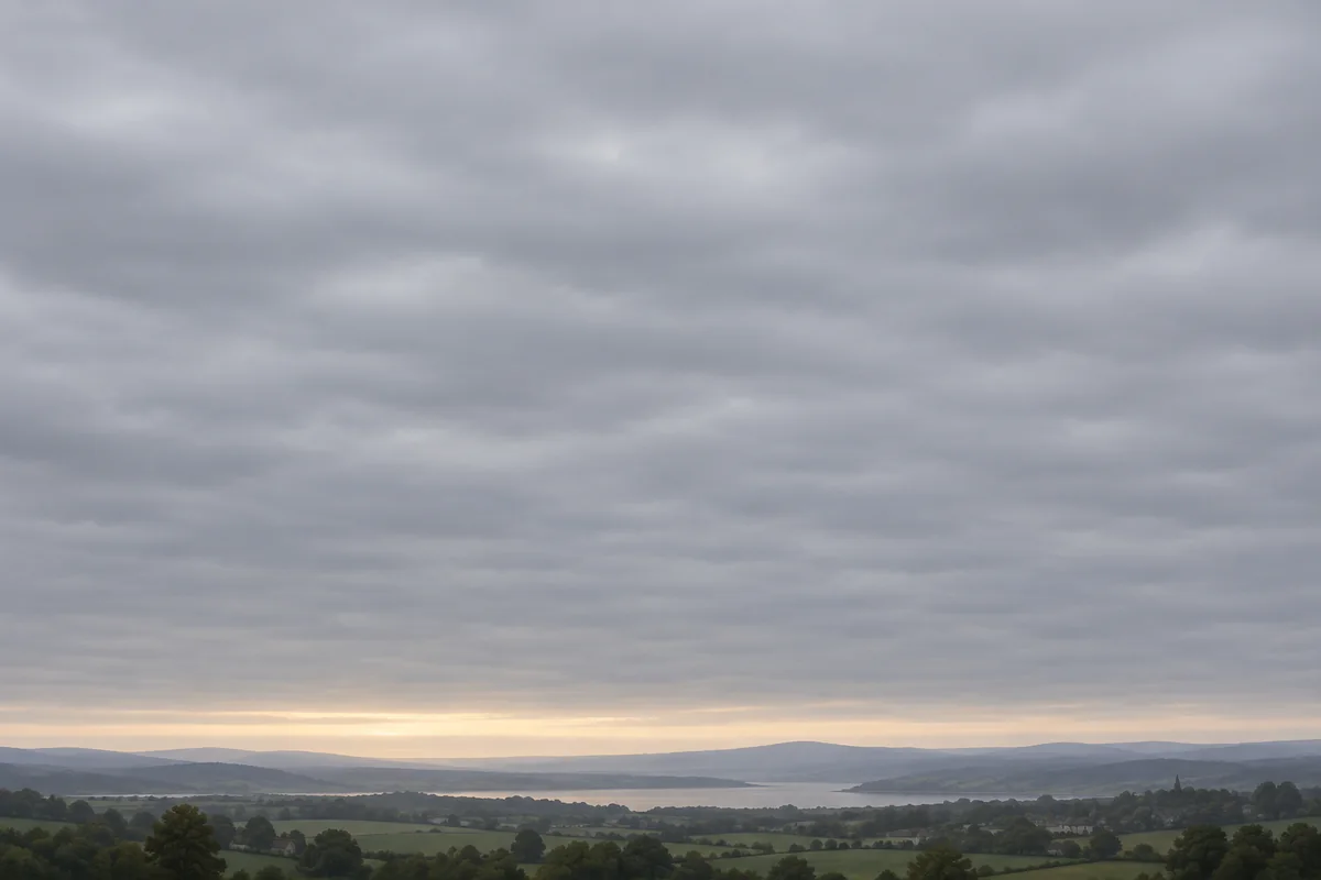 A wide, layered gray stratus cloud deck fills the sky while a soft band of sunlight appears near the horizon.
